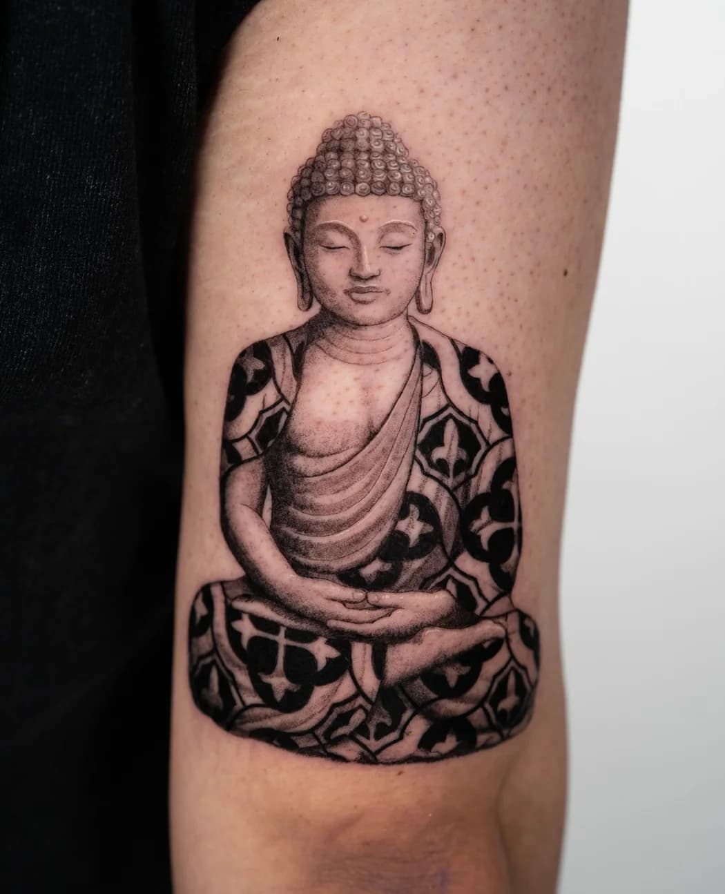 Seated buddha in a patterned robe on an upper arm